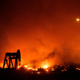 Smoke from the Maria Fire rises above an oil pumpjack as a helicopter passes overhead in the night.